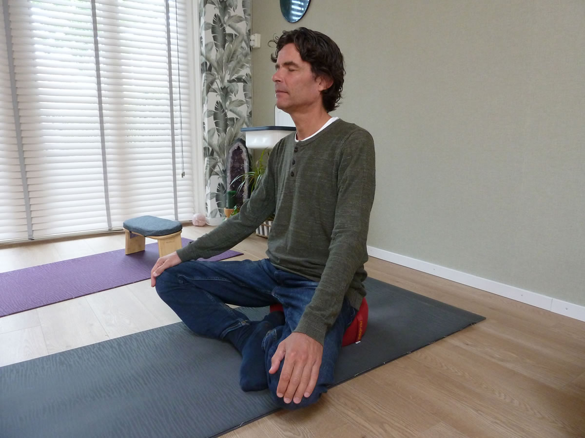 Zitten op een rood meditatiekussen, met de benen gekruist en de handen op de knieën