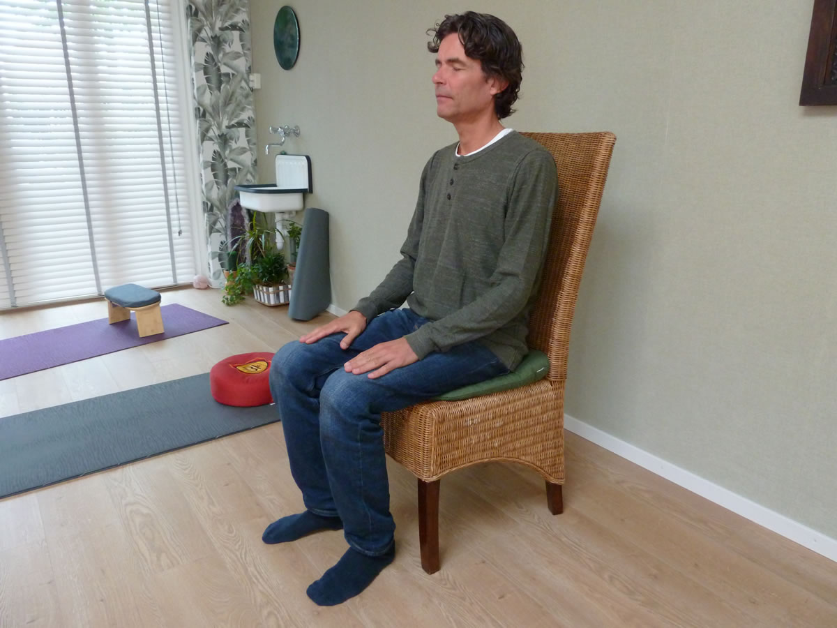 Meditatie op een stoel, met beide voeten op de grond en de handen op de bovenbenen