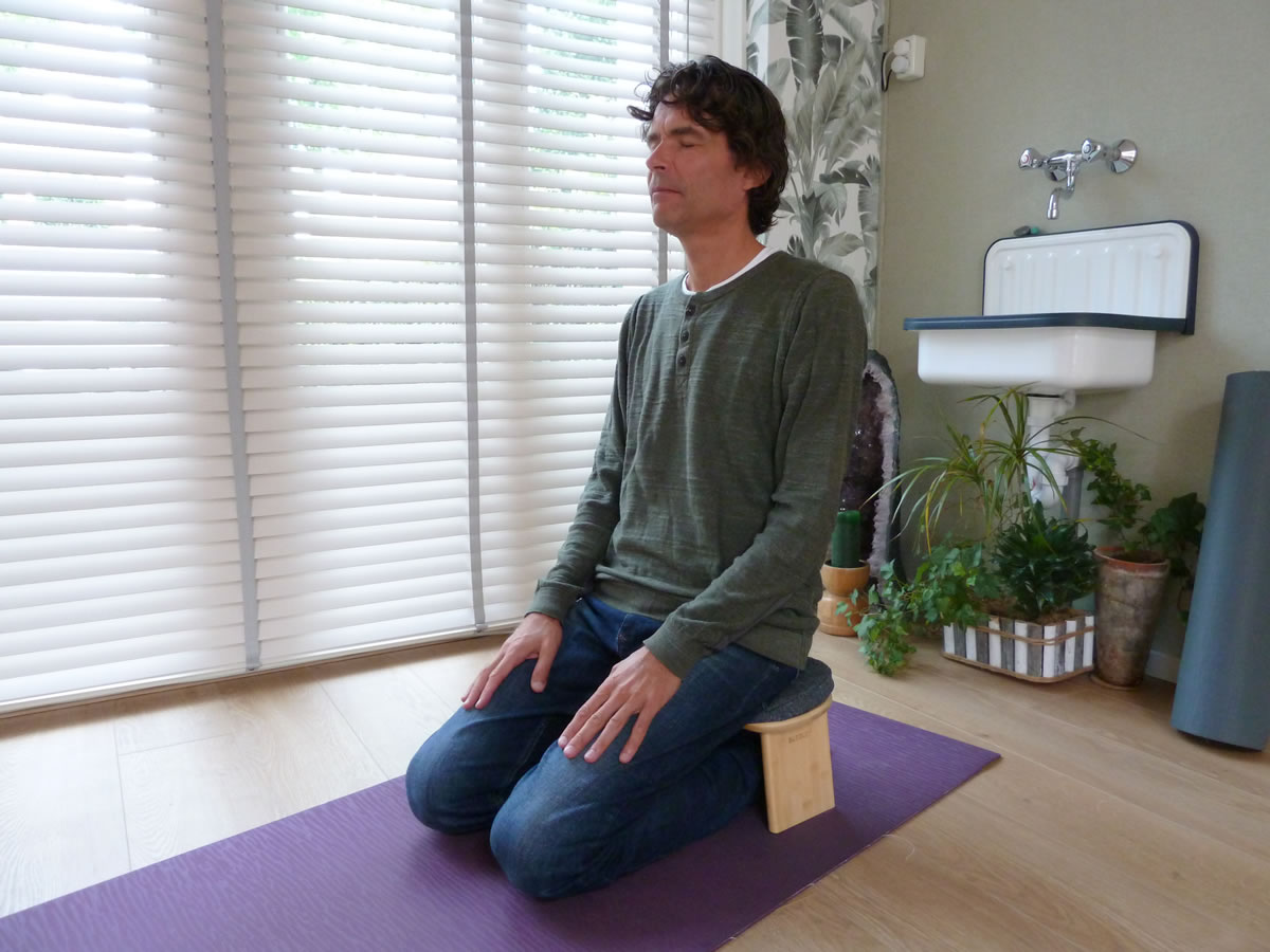 Knielhouding op een houten meditatiebankje, met de knieën op een paarse mat